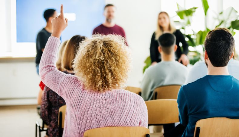 A woman raises her hand to ask a question during a presentation.