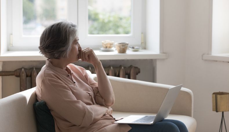 A woman pauses to think while working on her laptop at home.