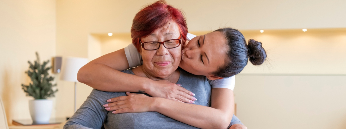 A daughter hugs her mother while providing care.