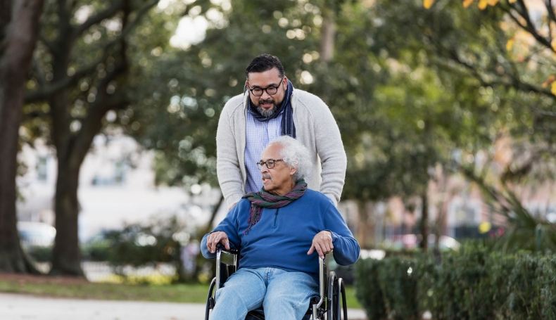 A son pushes his father's wheelchair during an afternoon walk.