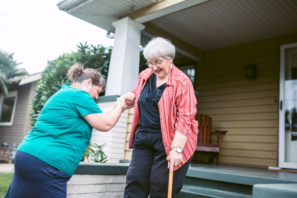Older adult with a cane being helped down steps by a caregiver.